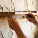 Un homme fixe avec précaution une étagère chargée sur un ancien mur en plâtre à l’aide d’outils et de chevilles adaptées.