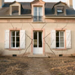 Façade d’une maison individuelle en France montrant des fissures obliques près des fenêtres, avec un jardin desséché après une période de sécheresse.